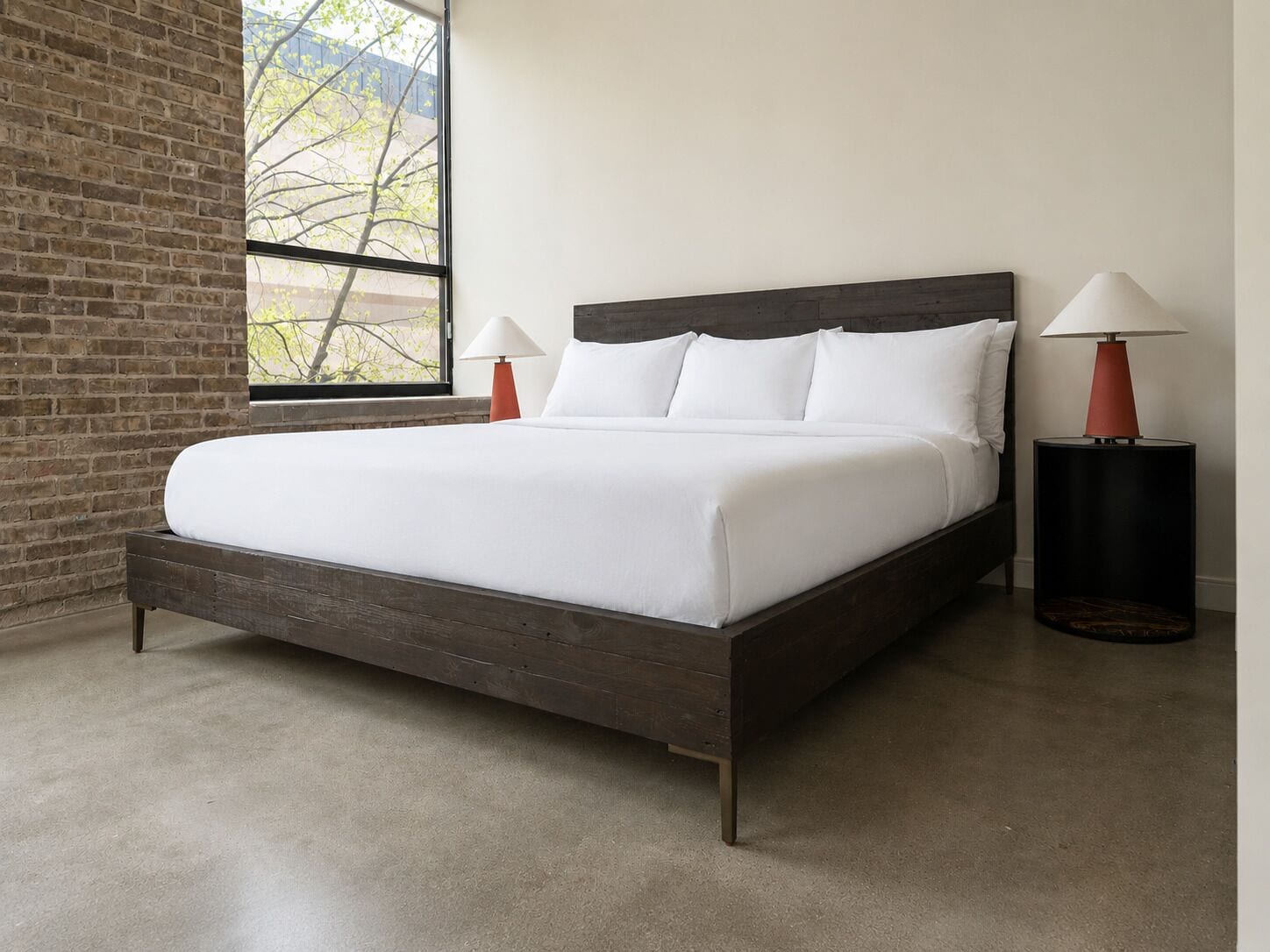 Un dormitorio moderno con un ventanal grande, una pared de ladrillo, un cabecero de madera y dos lámparas de noche.