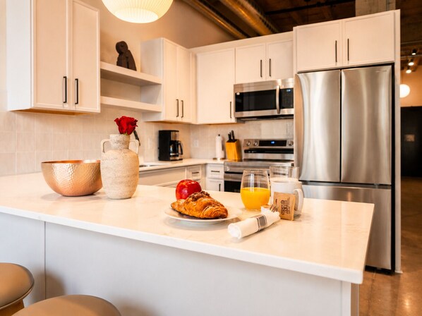 Una cocina moderna con armarios blancos, electrodomésticos de acero inoxidable y una isla central con un florero, un tazón y alimentos.