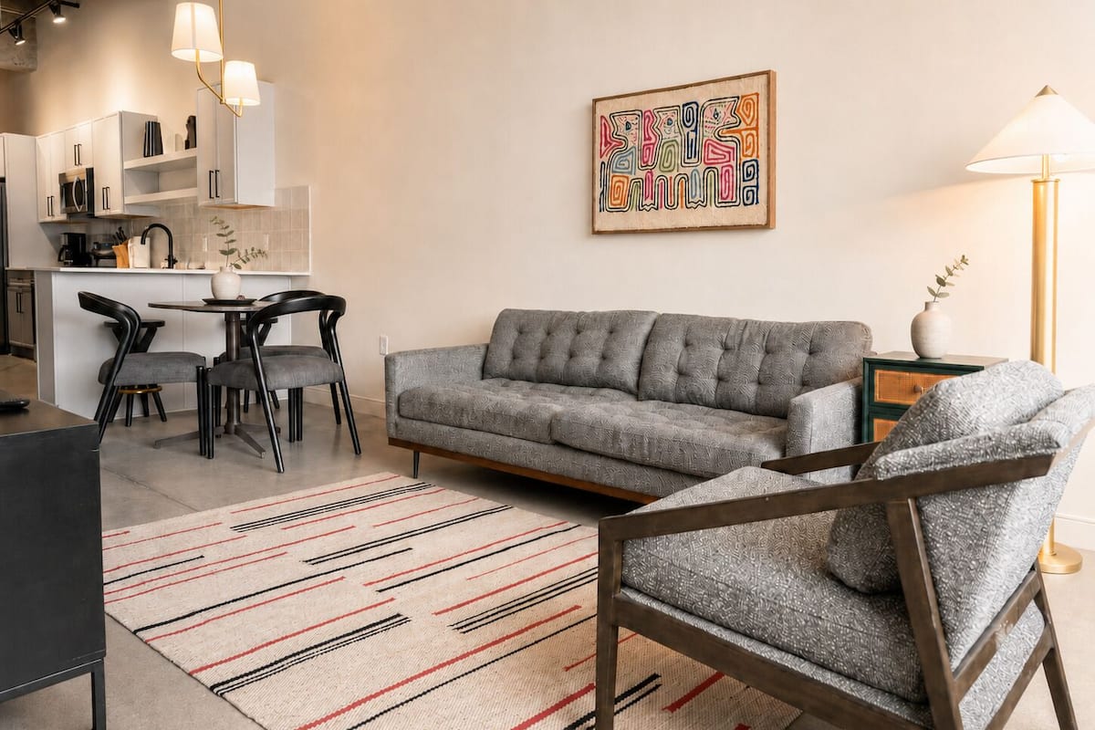 Een moderne woonkamer met een grijze bank, een gestreept vloerkleed en een eethoek met stoelen en een tafel.
