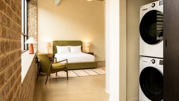 Una habitación de hotel con una cama, una silla, una lavadora y una pared de ladrillo.