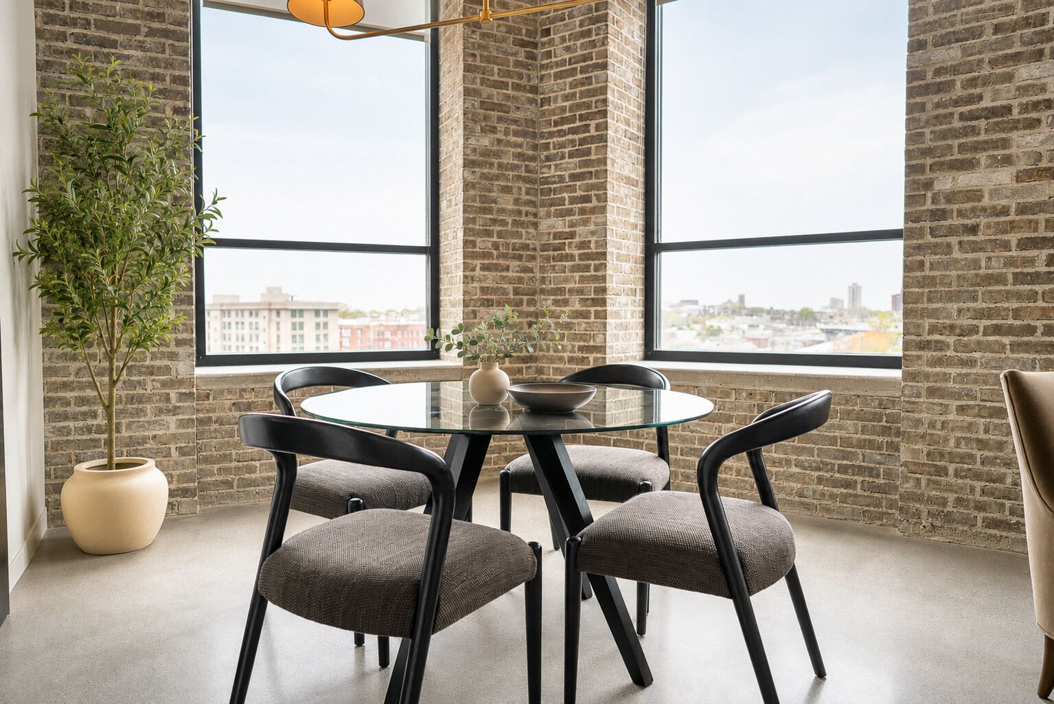 A modern meeting room with a glass table, black chairs, a potted plant, and a city view through large windows.
