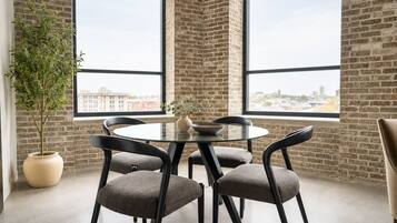 A modern meeting room with a glass table, black chairs, a potted plant, and a city view through large windows.