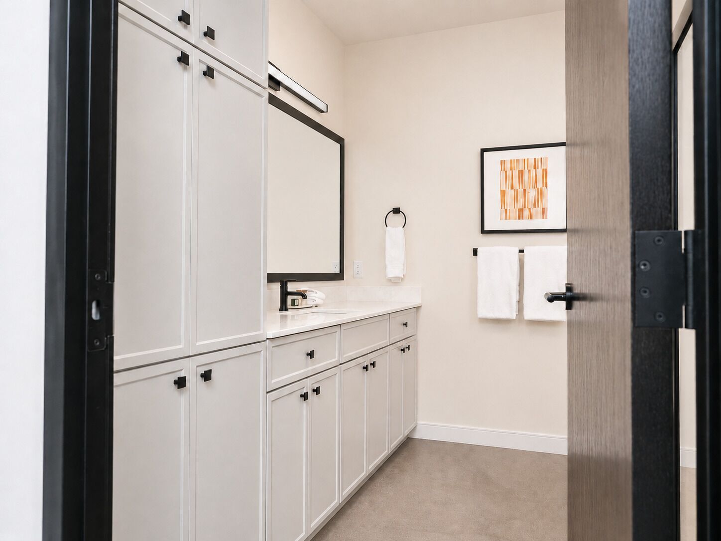 A bathroom with white cabinetry, a mirror, a towel rack, and a framed artwork on the wall.