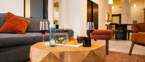 A modern living room with a grey sofa, a wooden coffee table with food and drinks, and a dining area in the background.