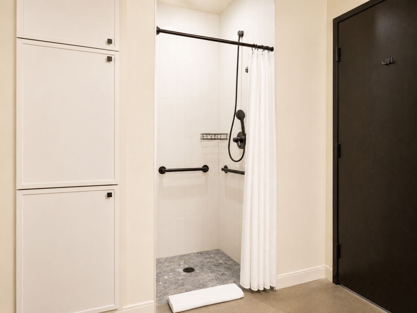 A shower with a tiled floor, a white towel, and a dark door.