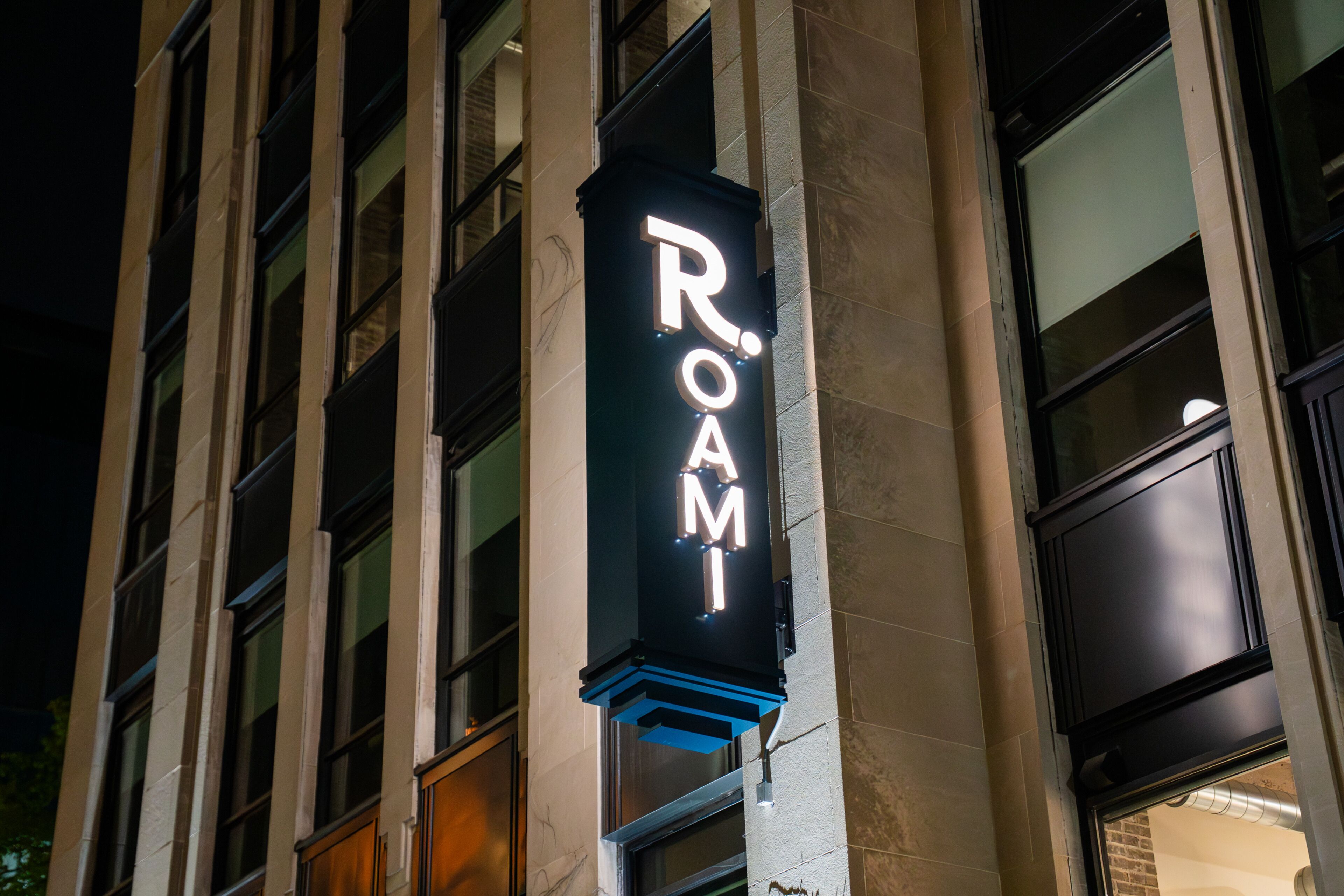 A building with a neon sign reading 'ROAMI' on the corner.