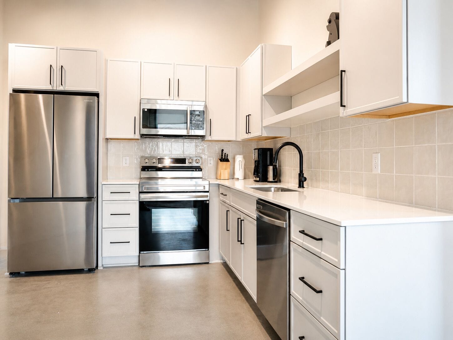 Una cocina moderna con electrodomésticos de acero inoxidable, armarios blancos y un grifo negro.