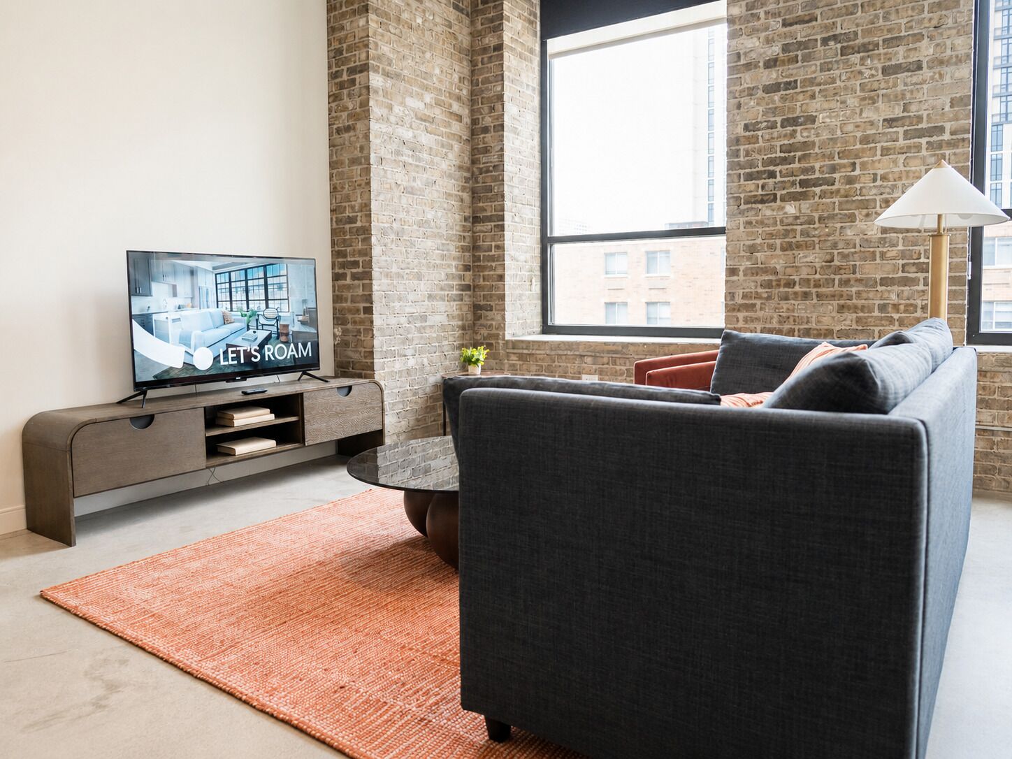 A modern living room with a grey sofa, a flat-screen TV, a coffee table, and a brick wall.