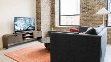 A modern living room with a grey sofa, a flat-screen TV, a coffee table, and a brick wall.