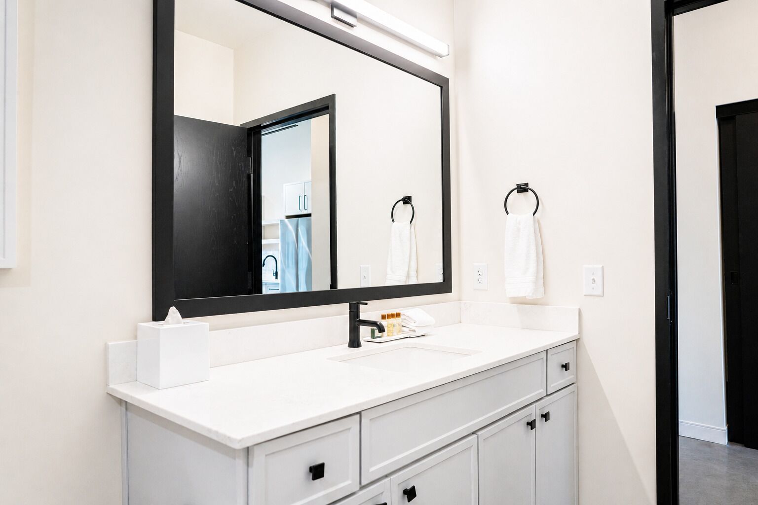 A modern bathroom with a white vanity, a large mirror, and a black-framed mirror.