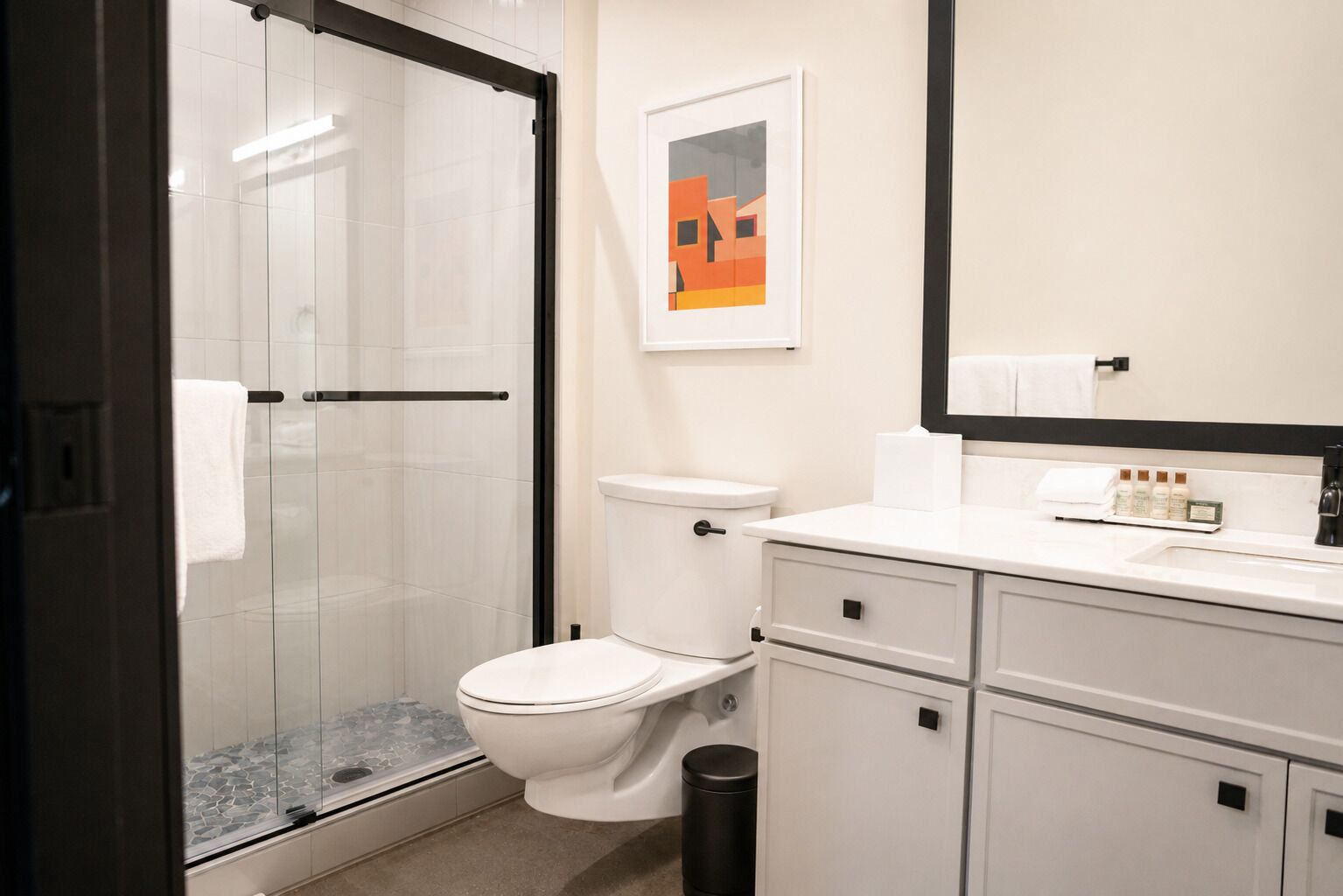 A modern bathroom with a glass shower enclosure, a toilet, a sink with toiletries, and a mirror.