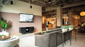 A modern lounge area with sofas, a TV, and a kitchen in the background.