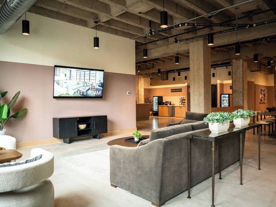 A modern lounge area with sofas, a TV, and a kitchen in the background.