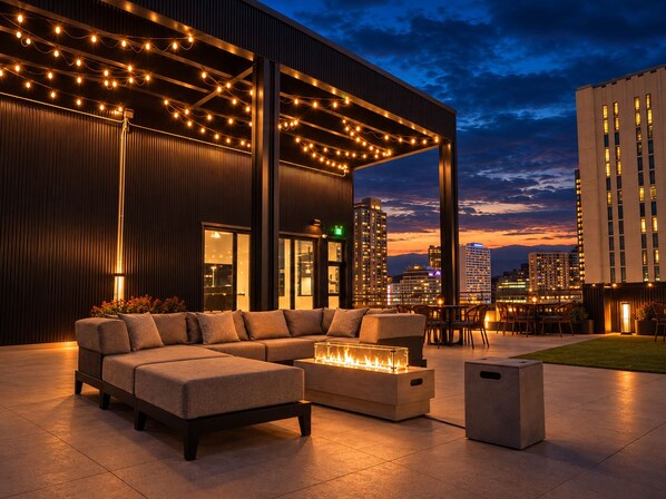 An outdoor seating area with a sofa, chairs, and a fire feature, overlooking a cityscape at dusk. - Roami at Century Plaza (Minneapolis)