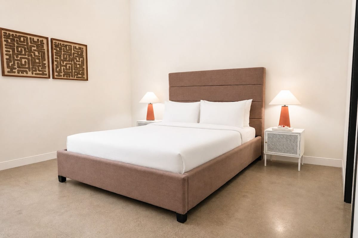 Een net opgemaakt bed met een hoofdeinde, twee nachtkastjes met lampen, en twee decoratieve wandpanelen.