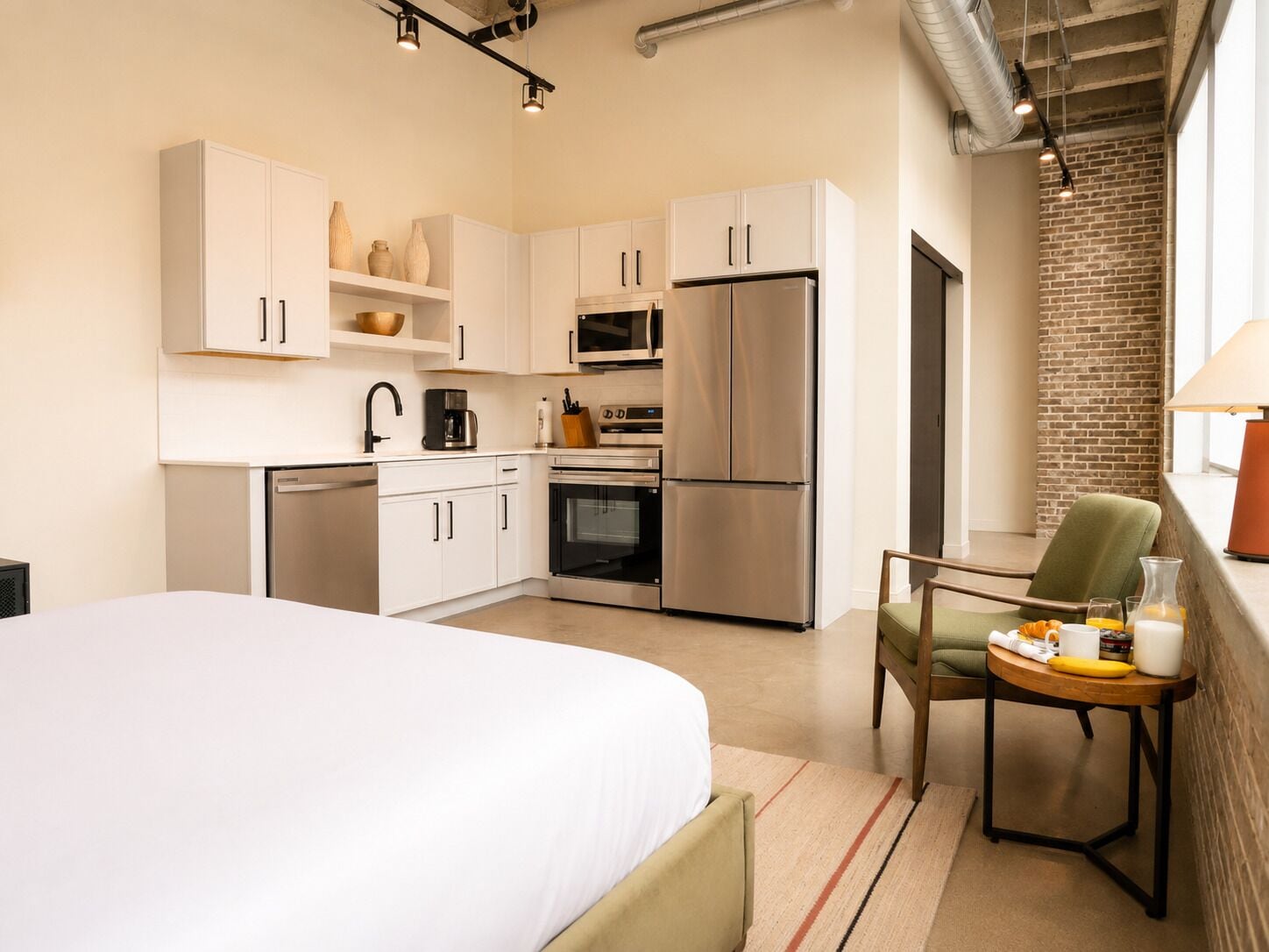 A compact hotel room with a bed, kitchenette, and a view of a brick wall.