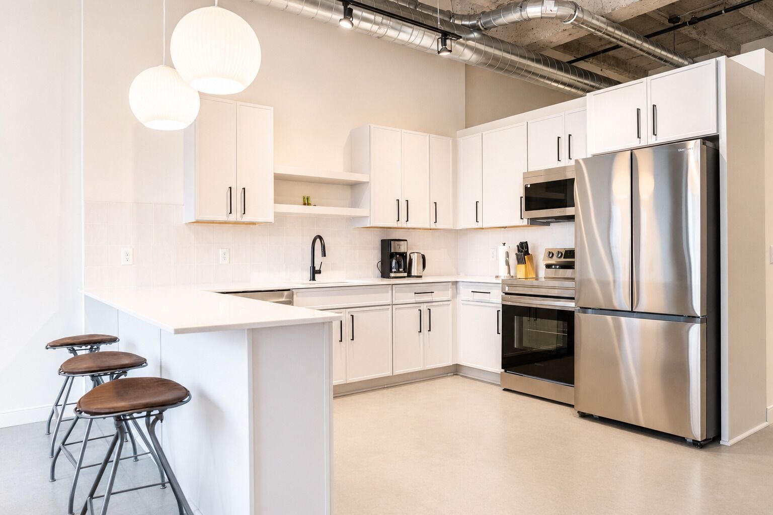 Una cocina moderna con armarios blancos, electrodomésticos de acero inoxidable y taburetes de bar.