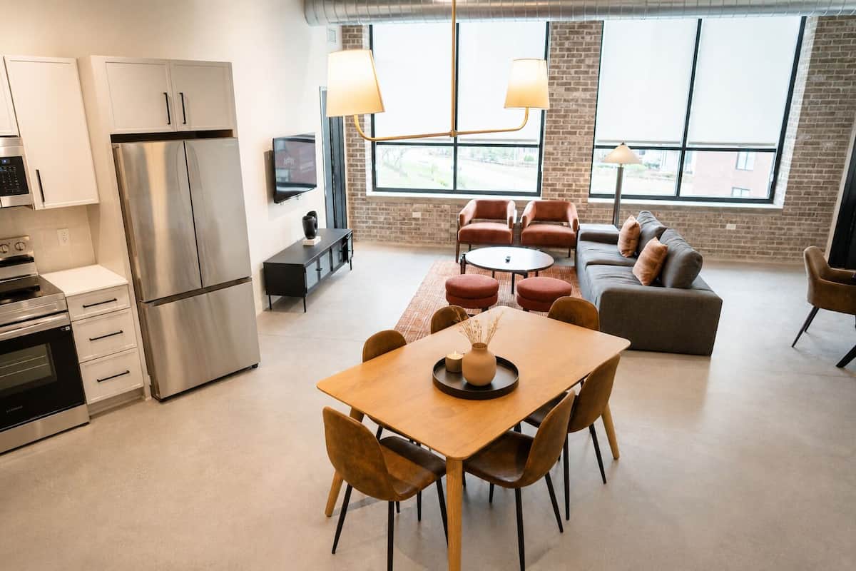 Een moderne keuken met roestvrijstalen apparatuur, een eethoek met een houten tafel en stoelen, en een zithoek met banken en fauteuils.