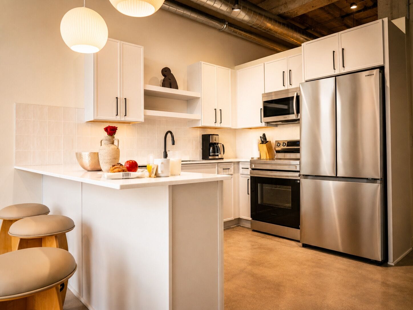 Una cocina moderna con armarios blancos, electrodomésticos de acero inoxidable y una isla central con asientos.