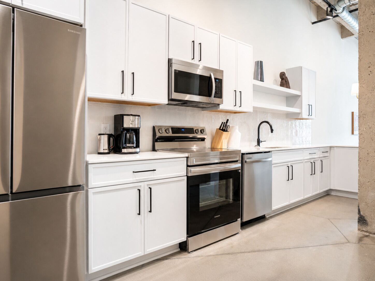 A modern kitchen with stainless steel appliances, white cabinetry, and a concrete floor.