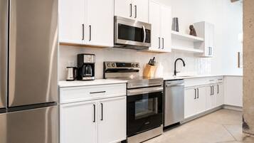 Una cucina moderna con elettrodomestici in acciaio inossidabile, mobili bianchi e pavimento in cemento.