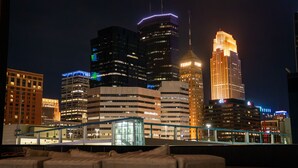 Un paisaje urbano nocturno con rascacielos iluminados y un edificio moderno con fachada de vidrio.