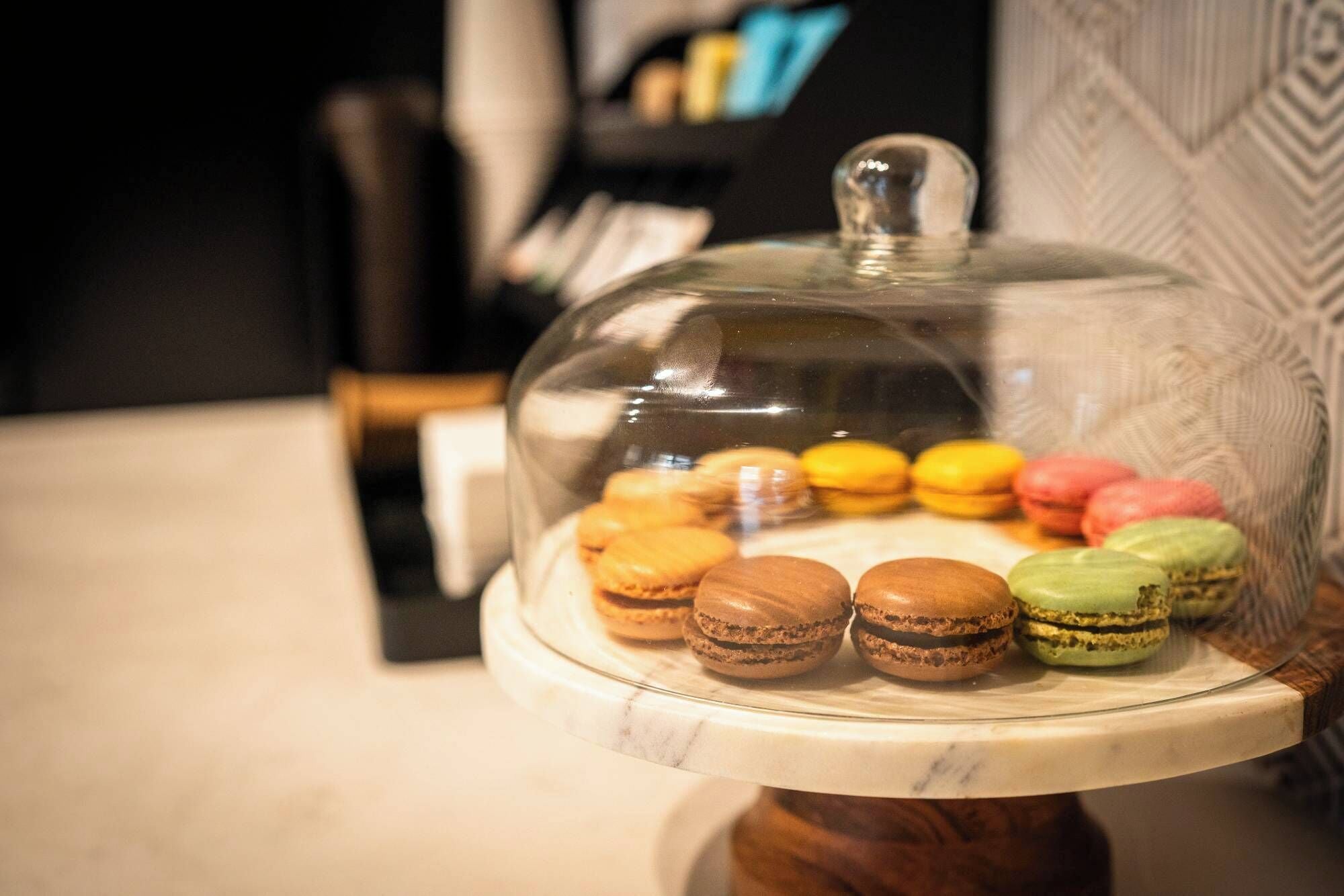 Exposição de macarons sob uma cobertura de vidro sobre um suporte de mármore.