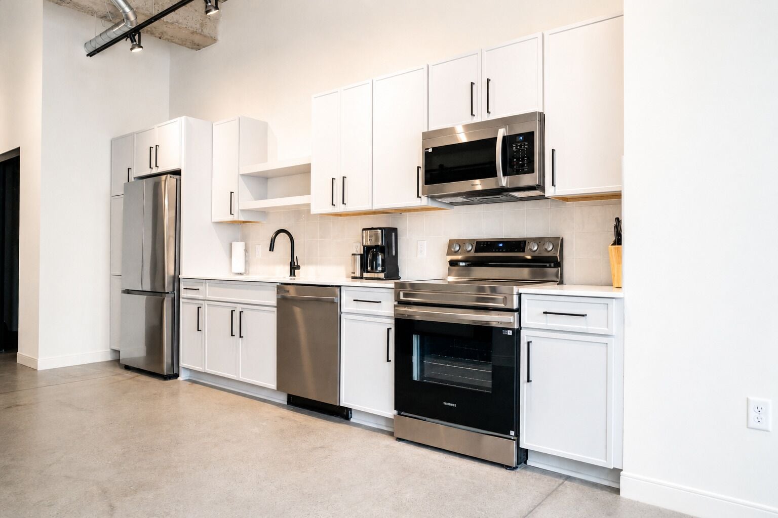 A modern kitchen with stainless steel appliances, white cabinetry, and a visible dishwasher.