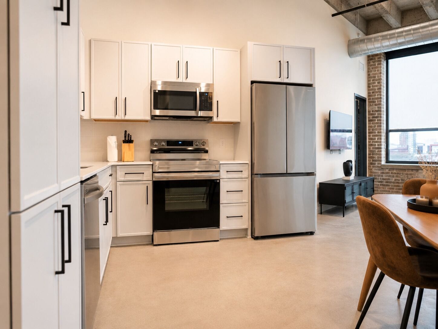 Een moderne keuken met roestvrijstalen apparatuur, witte kasten en een eethoek met een tafel en stoelen.