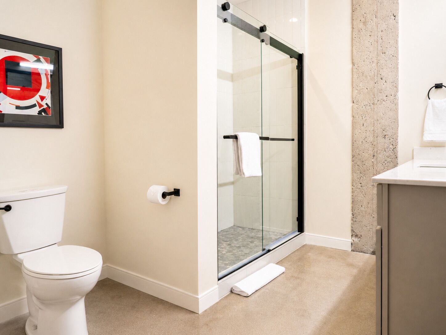 Une salle de bain moderne dotée d’une douche à parois de verre, de toilettes et d’un espace lavabo.