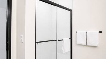 A glass-enclosed shower with a black frame, white tiled walls, and a towel rack with two white towels.