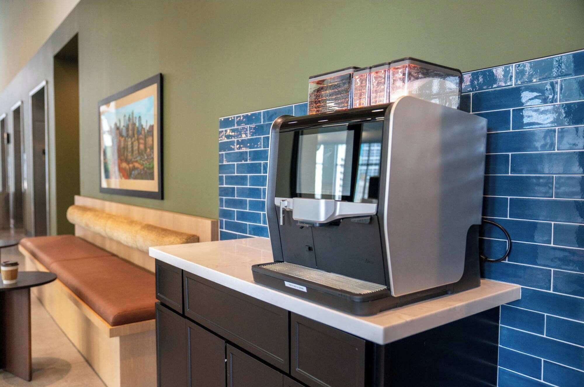 A coffee machine in a cafe with a blue-tiled wall and a bench.