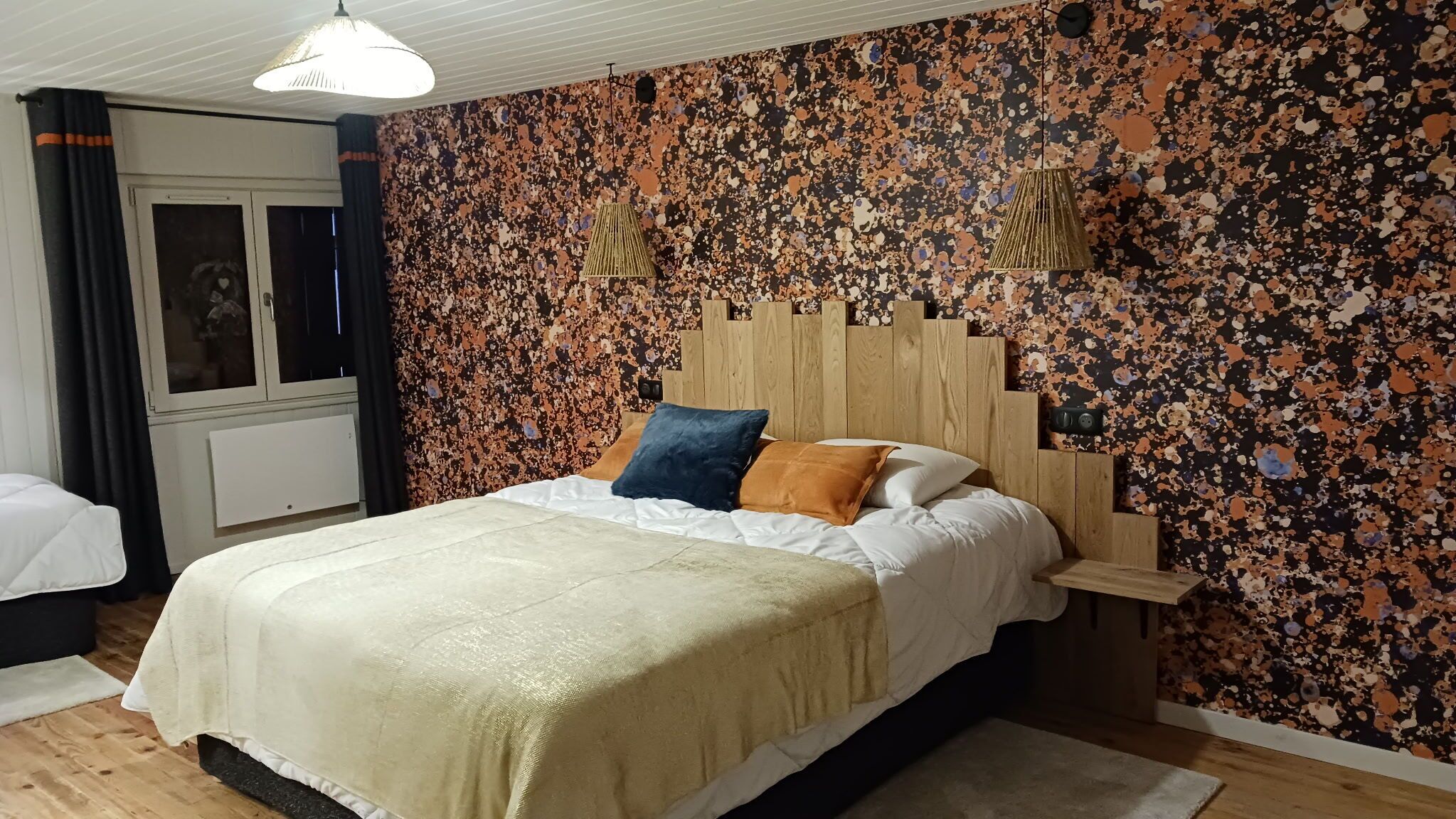 A bedroom with a bed, a wooden headboard, a window with curtains, and a wall with a speckled pattern.