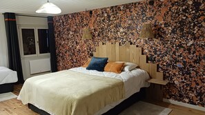 A bedroom with a bed, a wooden headboard, a window with curtains, and a wall with a speckled pattern. - Maison de village dans une belle vallée paisible à découvrir. (Le Pontet)
