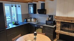 A modern kitchen with dark cabinetry, a tiled backsplash, a built-in microwave, and a wood-burning stove.