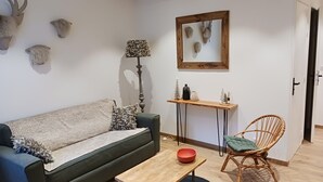 A living room with a sofa, a small table, a chair, a lamp, a console table with decorative items, and wall-mounted animal heads.