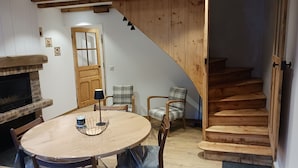 A dining area with a round table, chairs, a fireplace, and a wooden staircase.