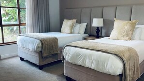 Ett hotellrum med två sängar, ett stort fönster och utsikt över grönområden.