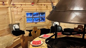 A wooden interior with a round table set for dining, a hanging lamp, and a window with a view of trees.