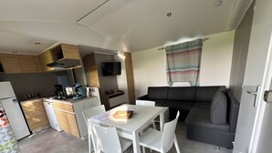 A compact kitchen with a dining table and chairs, a black sofa, and a TV mounted on the wall.