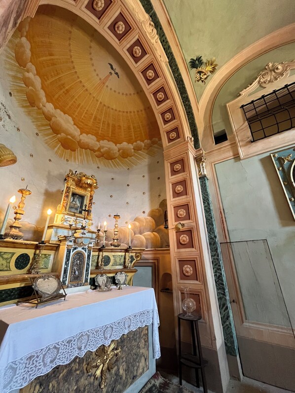 An ornate room with a high ceiling, a table with a white tablecloth, and a decorative altar. - Agriturismo Villa La Fontina (Castiglion Fiorentino)