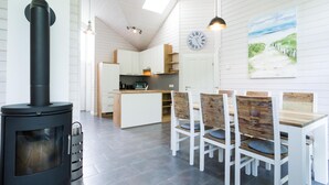 A modern kitchen with a stove, dining table, chairs, and a clock on the wall. - Ferienhaus in Schönberg-Holm: Sauna, Kamin & Strandkorb inklusive (Schönberg (Holstein))