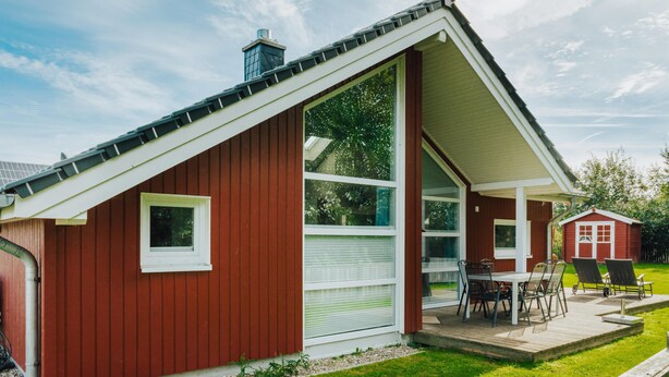 A red building with a large window and a patio with a table and chairs. - Ferienhaus in Schönberg-Holm: Sauna, Kamin & Strandkorb inklusive (Schönberg (Holstein))