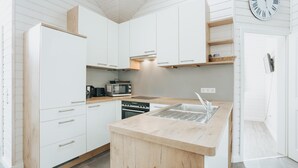 A modern kitchen with white cabinets, a wooden countertop, a built-in oven, a microwave, and a sink. - Ferienhaus in Schönberg-Holm: Sauna, Kamin & Strandkorb inklusive (Schönberg (Holstein))