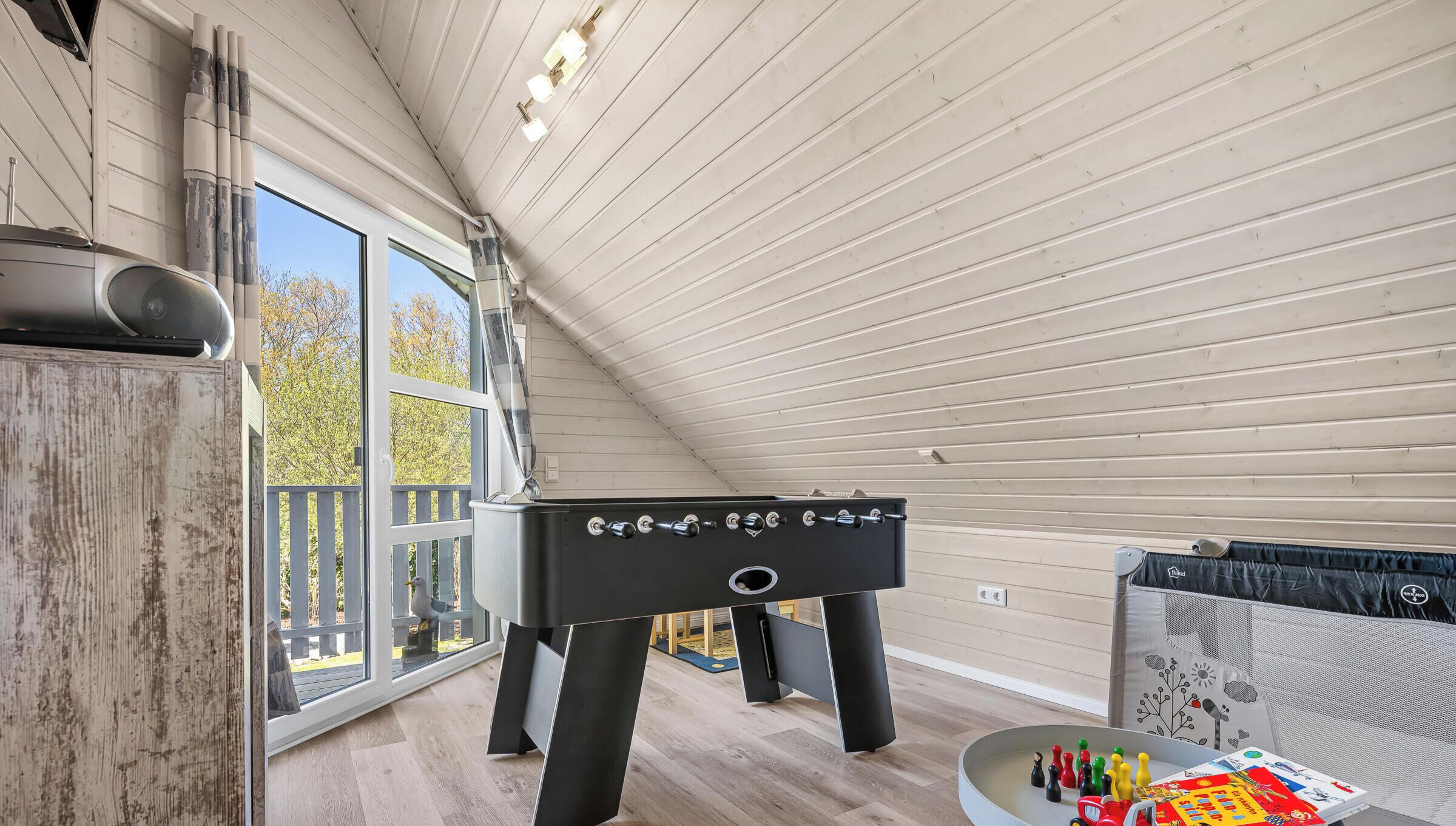Quarto com mesa de futebol de mesa, janela com vista para árvores e teto de madeira.