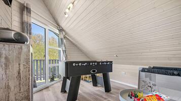 Quarto com mesa de futebol de mesa, janela com vista para árvores e teto de madeira.