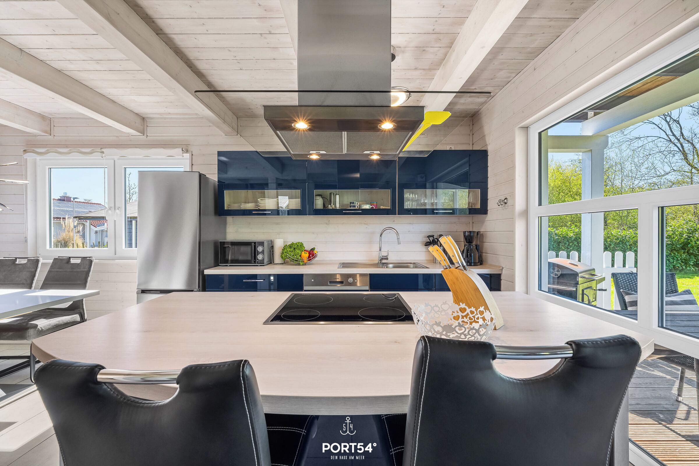 Una cocina moderna con una isla central, electrodomésticos de acero inoxidable y ventanas amplias.