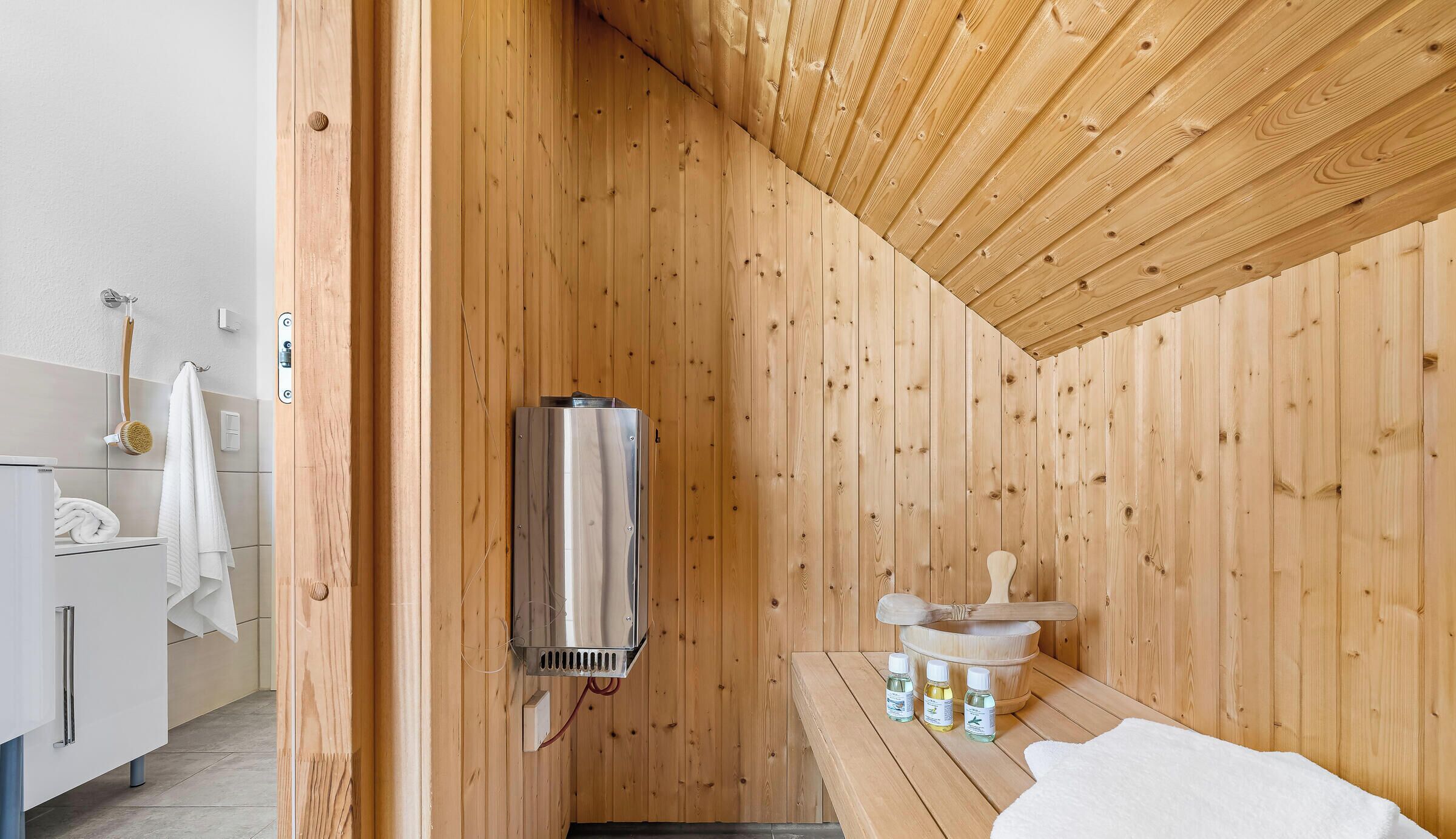 A sauna room with wooden walls, a bench, a massage table, and bottles of oils.