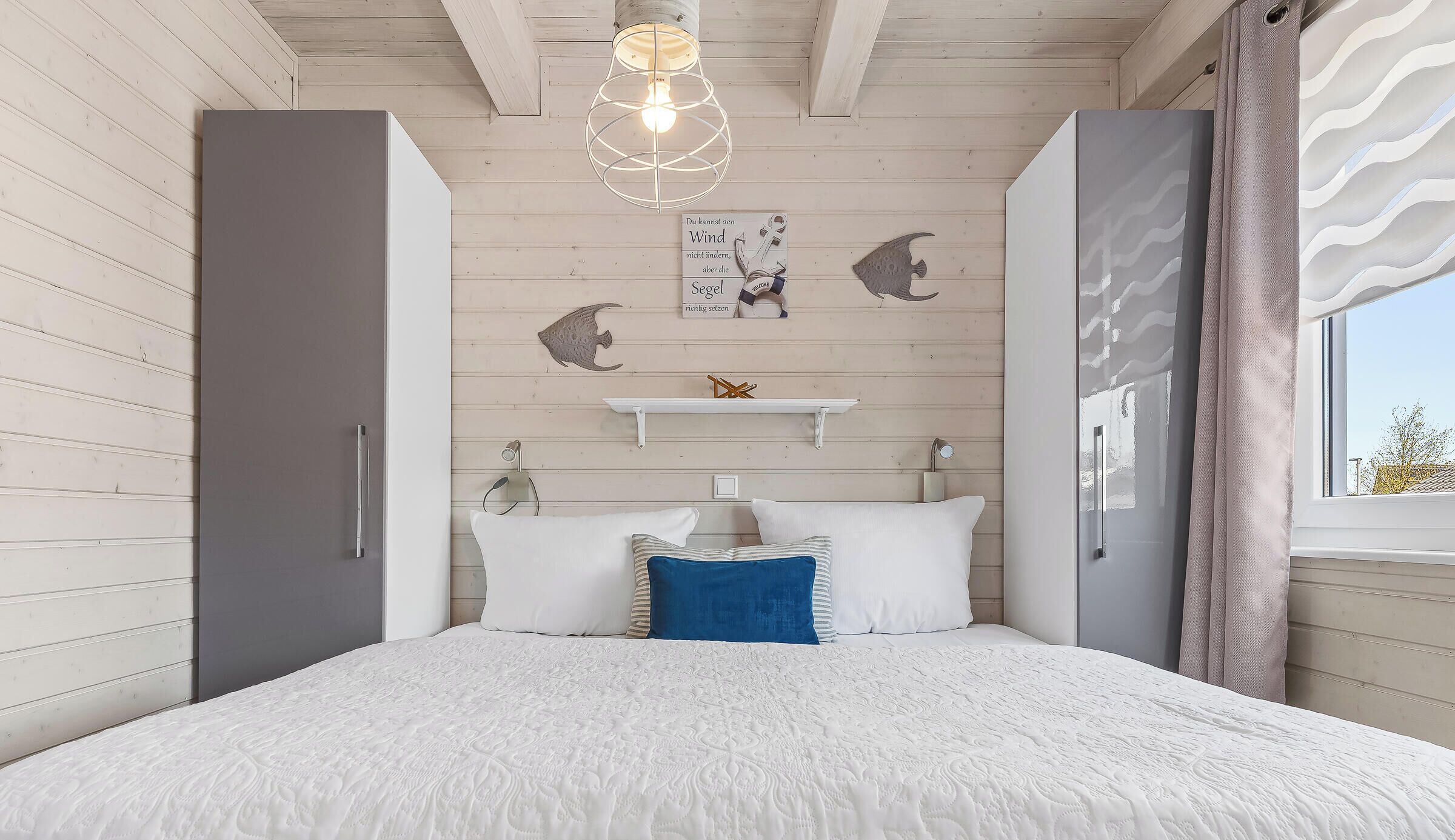 Ein Schlafzimmer mit einem Bett, einer Pendelleuchte, einem Regal mit Dekorationen und einem Fenster mit Vorhängen.