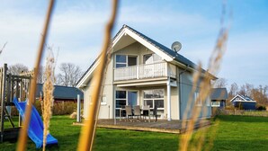 Ett tvåvåningshus med en balkong, en uteplats med utemöbler och en blå rutschkana på gården.